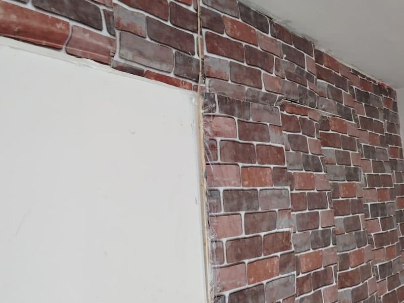 Interior wall space featuring poorly applied brick-effect wallpaper with visible seams and misalignment, requiring cosmetic attention.