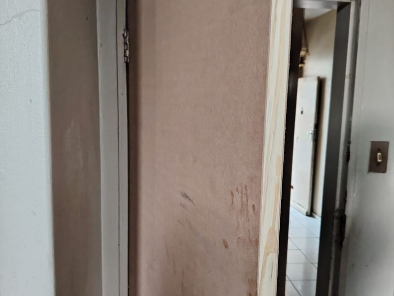 A hallway view featuring an unfinished wooden door with a metal handle, showing signs of wear and requiring finishing.