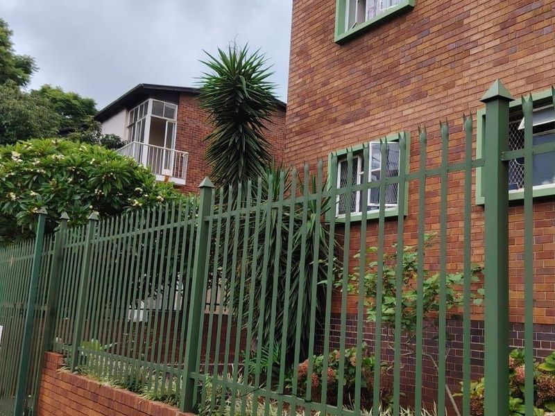 Exterior view of a face brick apartment building featuring secure metal fencing and burglar bars on the windows.