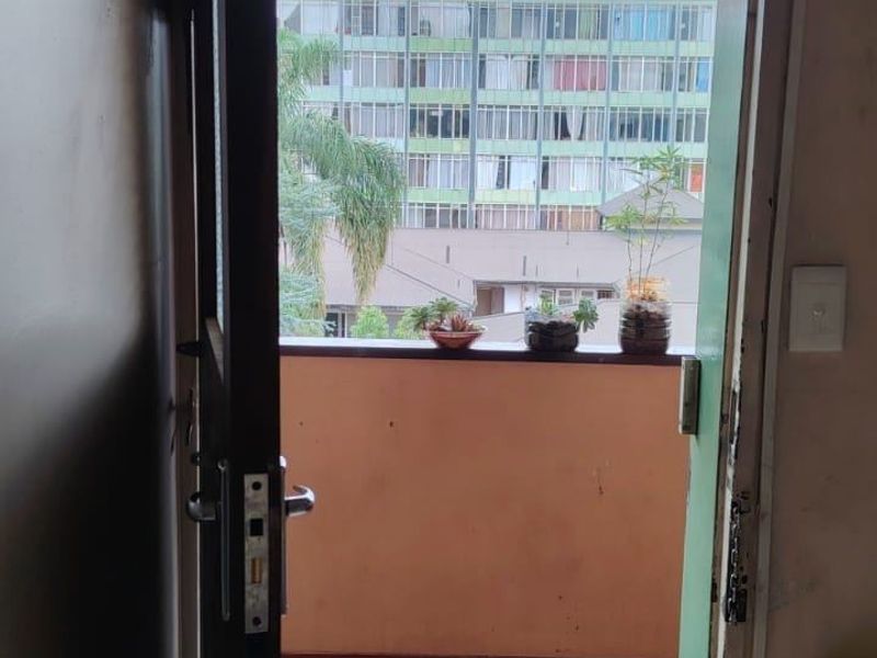 A view from an interior doorway looking out onto a small balcony with tiled flooring and a metal railing, overlooking a neighboring apartment building.