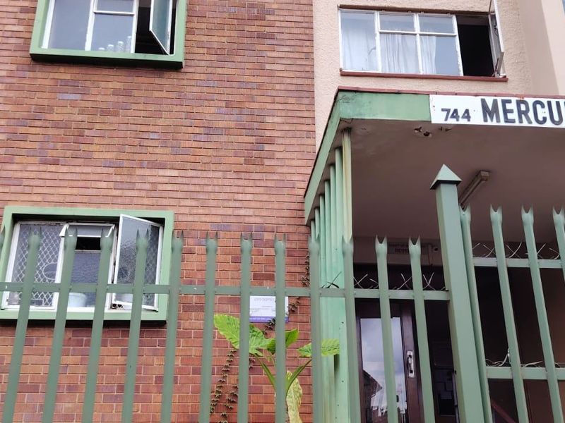 Front exterior view of the Mercury apartment building, featuring a brick facade, metal security fencing, and a concrete entrance canopy.