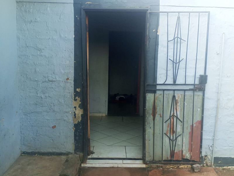 Front entrance of the property featuring a security gate, tiled interior flooring, and exterior masonry walls showing signs of wear and peeling paint.
