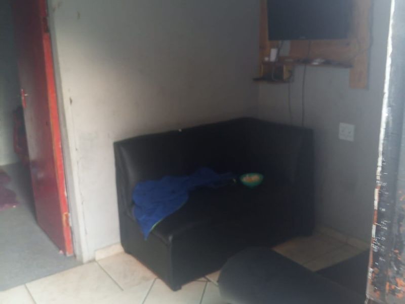 A compact living area featuring tiled flooring and a wall-mounted television setup, requiring cosmetic updates to improve the overall aesthetic.