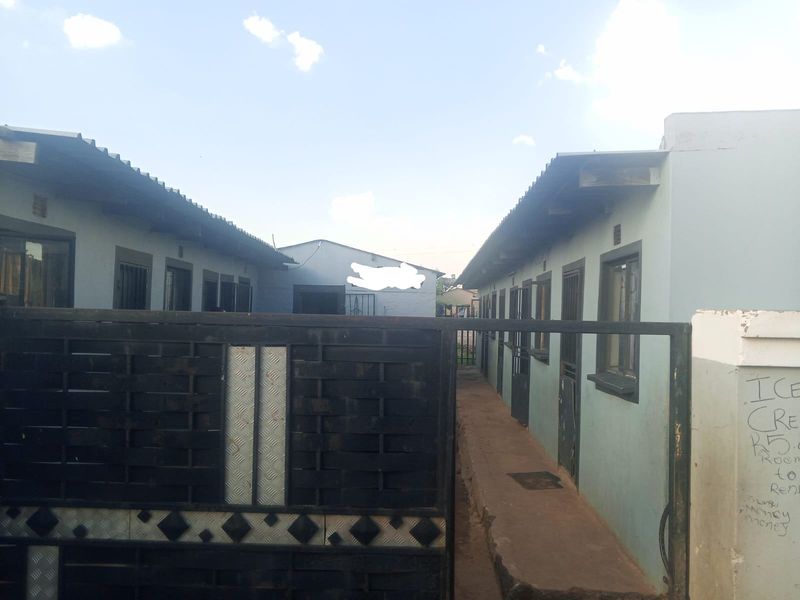 Exterior view of a residential property featuring a metal security gate, concrete walkway, and multiple unit entrances with security bars.