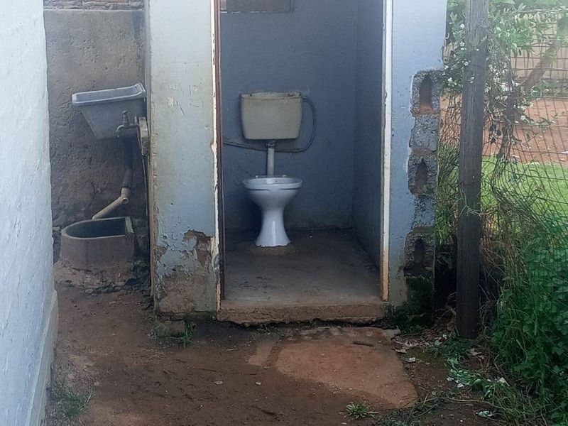 An outdoor utility structure featuring a basic toilet and external sink, showing significant signs of wear and structural deterioration.