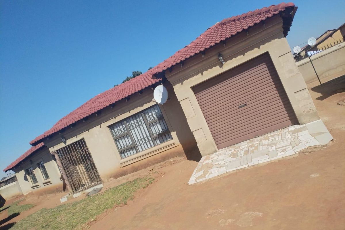 Front exterior view of a single-story house featuring a tiled roof, integrated garage with a roller door, and security fixtures on windows and doors.