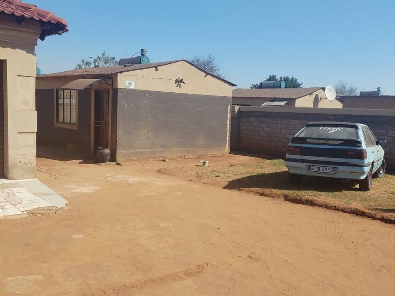 Rear exterior view of the property featuring a solar water heater, boundary wall, and unpaved yard area.
