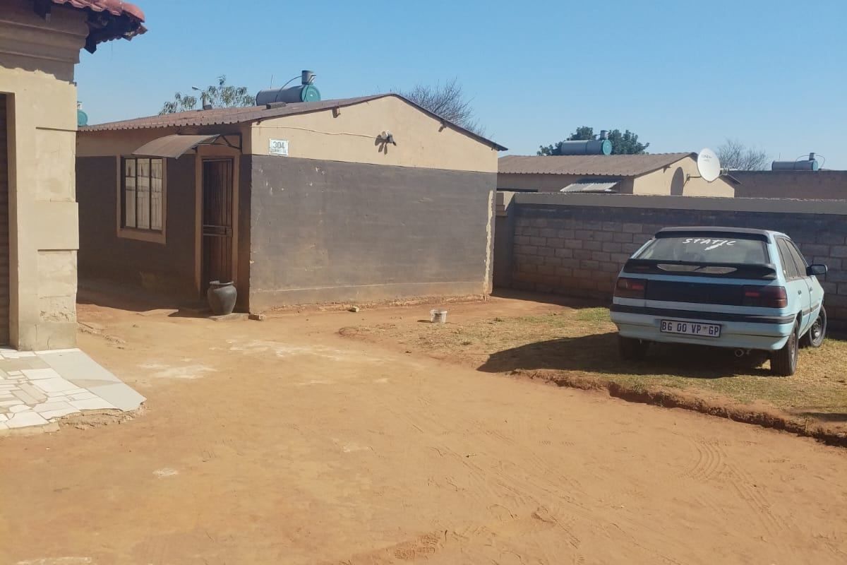 Rear exterior view of the property featuring a solar water heater, boundary wall, and unpaved yard area.
