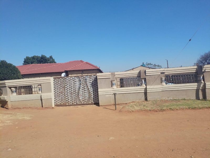 Front view of the property featuring a secure perimeter wall, metal driveway gate, and a tiled roof structure.