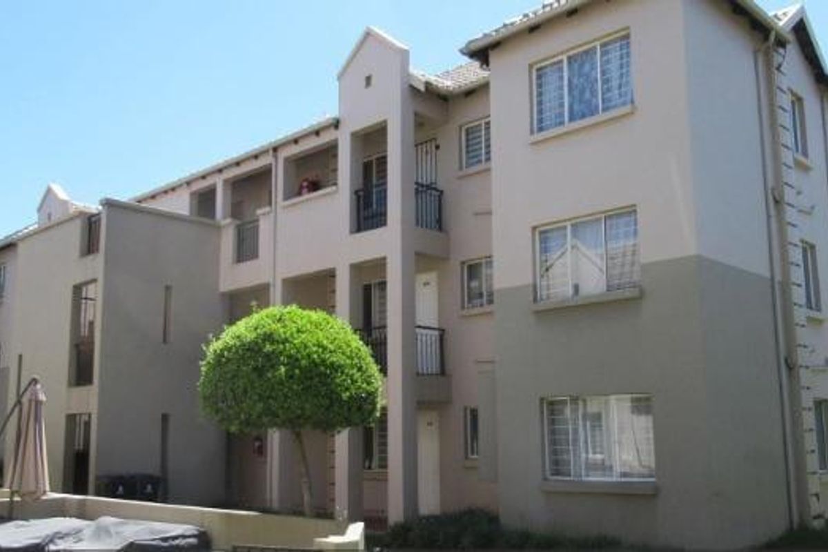 A multi-story apartment building exterior featuring balconies, security bars on windows, and a landscaped garden area.