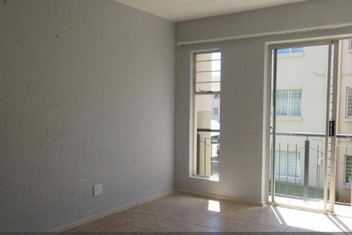 An empty living room featuring tiled flooring and a sliding glass door leading to a balcony, with neutral wall finishes.