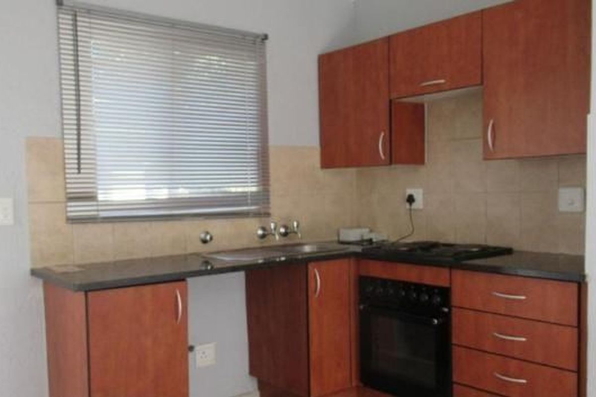 A functional kitchen featuring wood-finish cabinetry, granite countertops, a built-in oven with gas hob, and a tiled backsplash.