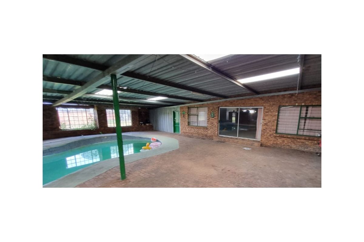 Covered indoor swimming pool area featuring a brick-walled enclosure, metal roofing, and paved surround, providing a sheltered space for year-round recreation.