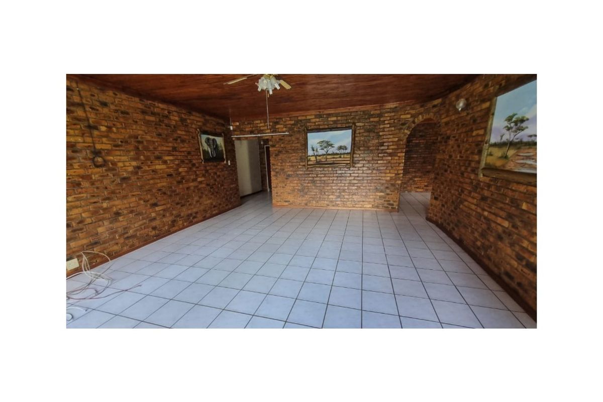 Spacious living area featuring exposed face-brick walls, tiled flooring, and a timber-clad ceiling with a central fan.