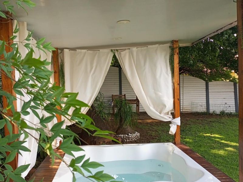 A private outdoor jacuzzi set within a timber deck under a covered pergola, situated in a landscaped garden setting.
