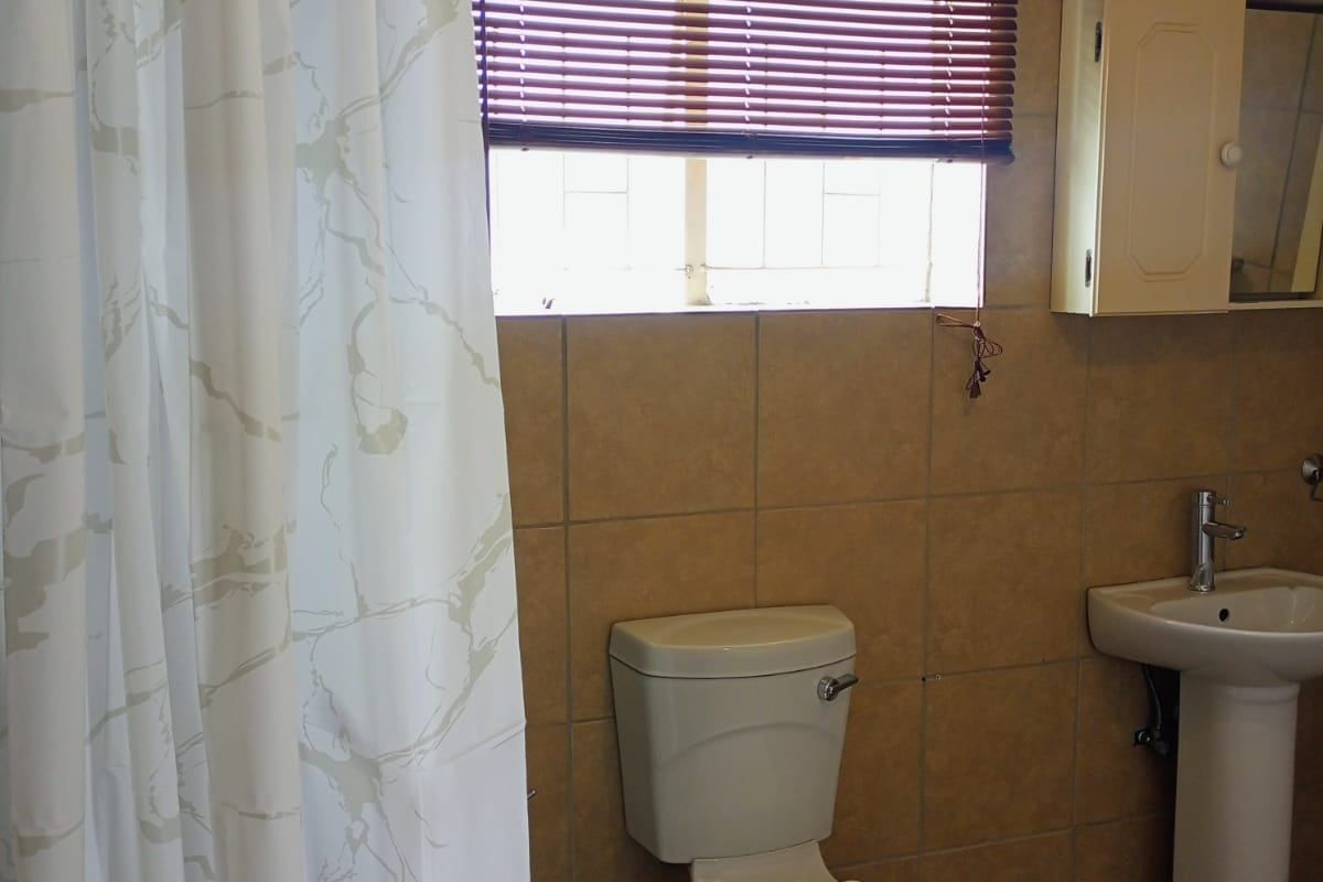 A functional bathroom featuring a pedestal sink, toilet, and tiled finishes, offering a neutral base ready for modern updates.