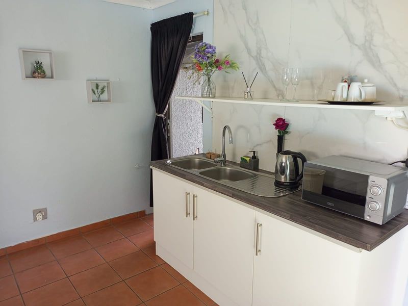 A compact kitchen area featuring white cabinetry, a stainless steel sink, and a marble-effect splashback, finished with terracotta floor tiles.
