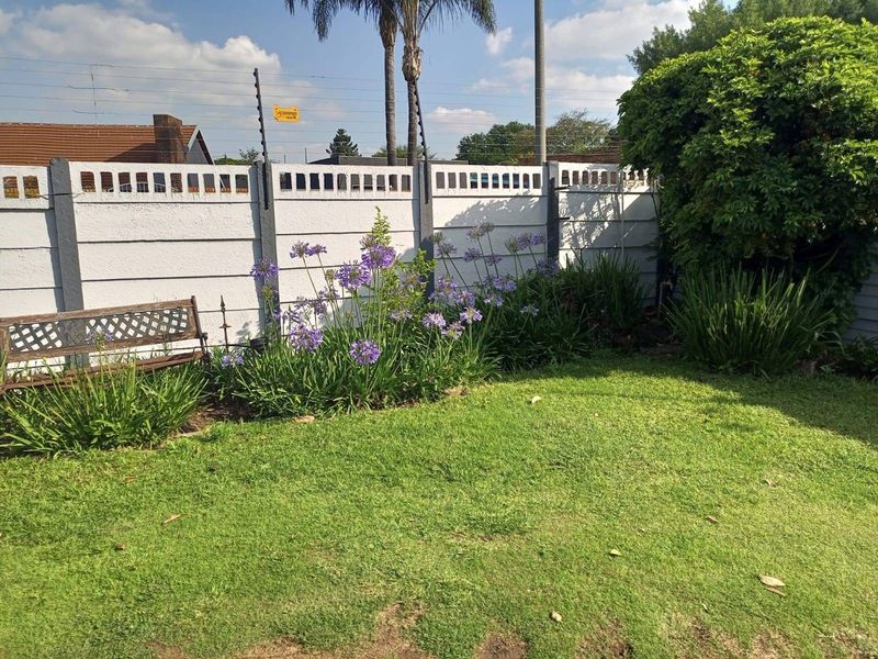 A well-maintained private garden featuring a manicured lawn, established flower beds, and a secure boundary wall equipped with electric fencing.