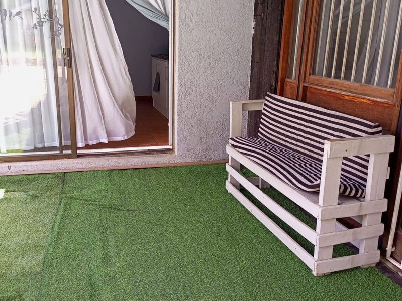 A covered patio area featuring artificial grass flooring, a timber pergola structure, and sliding glass door access to the interior living space.