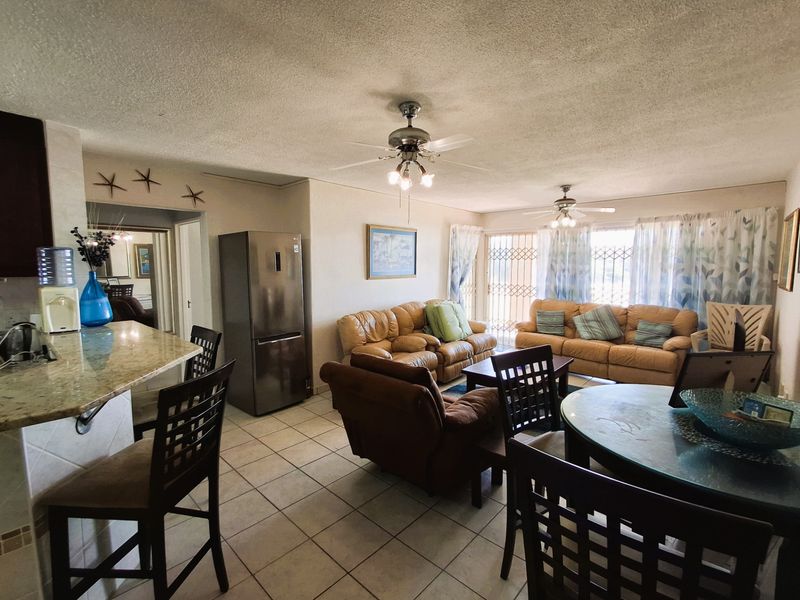 Open-plan living and kitchen area featuring tiled flooring, granite countertops, and dual ceiling fans with access to an outdoor balcony through a security gate.