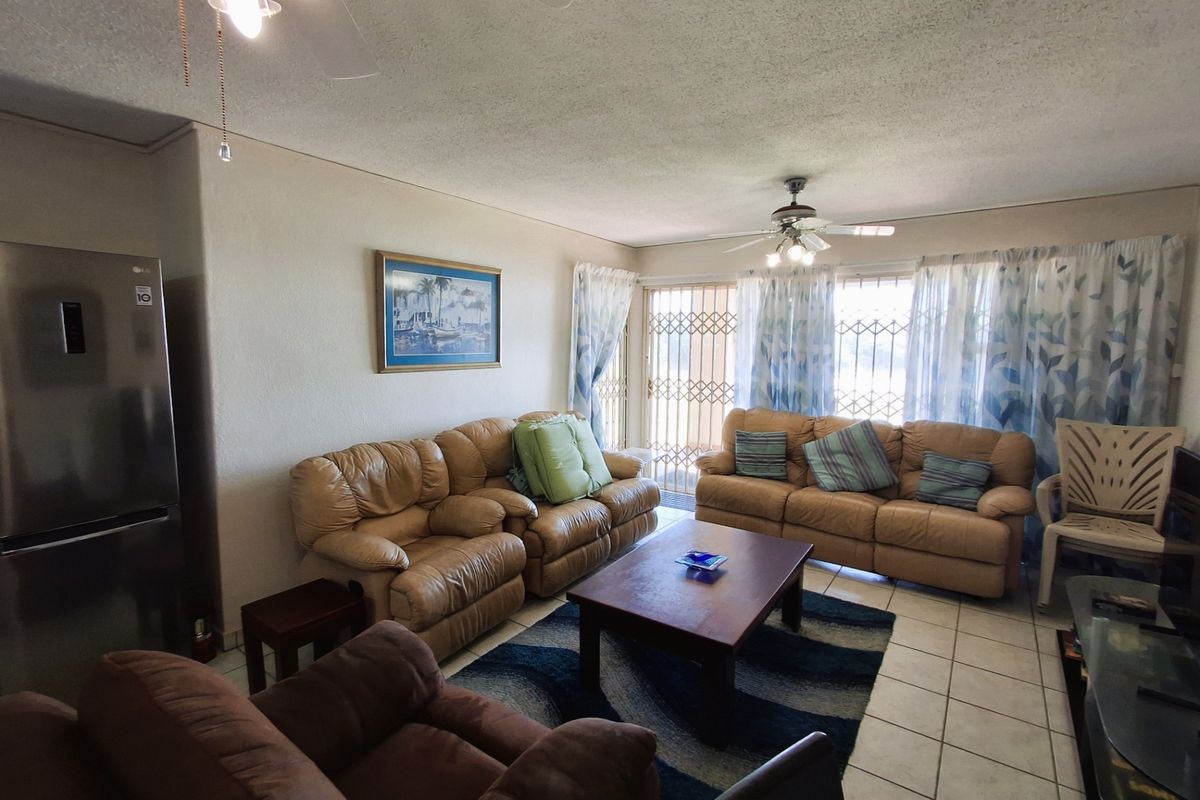 A living room featuring tiled flooring, ceiling fans, and a sliding door with a security gate leading to the exterior.