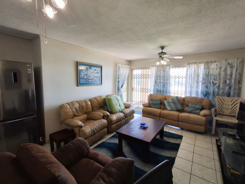 A living room featuring tiled flooring, ceiling fans, and a sliding door with a security gate leading to the exterior.