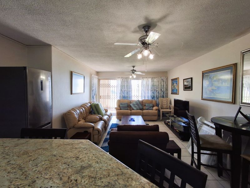 Open plan living area featuring tiled flooring, ceiling fans, and a granite breakfast bar, leading to a balcony with a security gate.