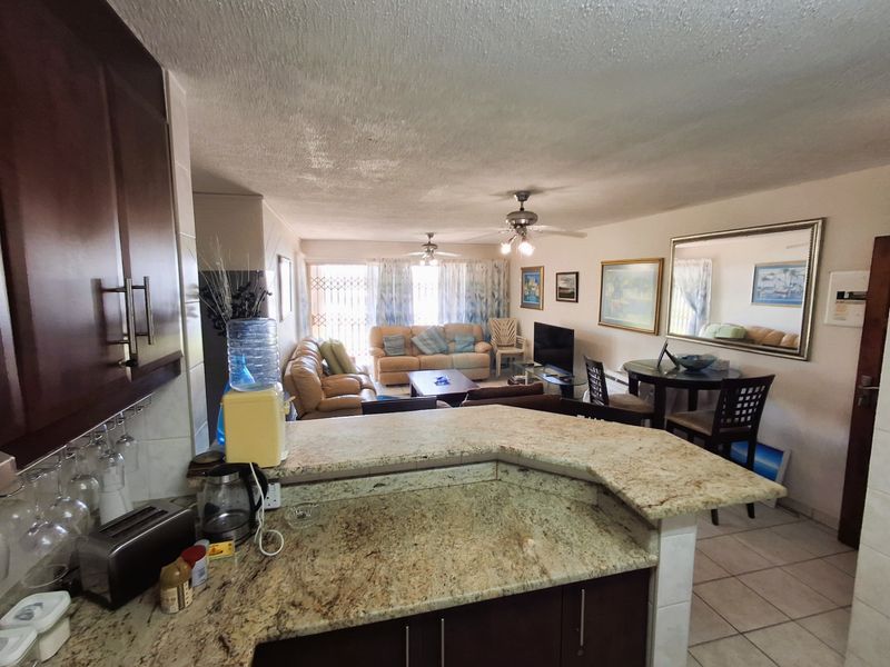Open-plan living and kitchen area featuring granite countertops, dark wood cabinetry, tiled flooring, and ceiling fans, leading to a balcony with security gate.