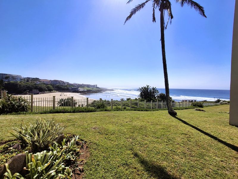 A scenic coastal view overlooking the beach and ocean, featuring a well-maintained lawn and perimeter fencing.