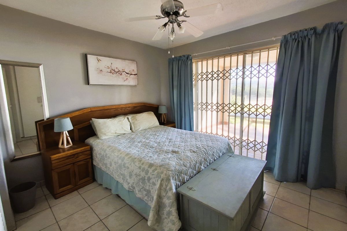 A bedroom featuring tiled flooring, a ceiling fan, and a sliding glass door with a security gate leading to an outdoor area.