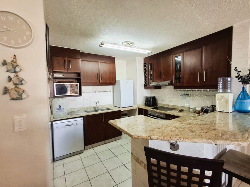 Functional kitchen featuring dark wood cabinetry, granite countertops, a breakfast bar, and tiled finishes, providing a practical layout for daily meal preparation.