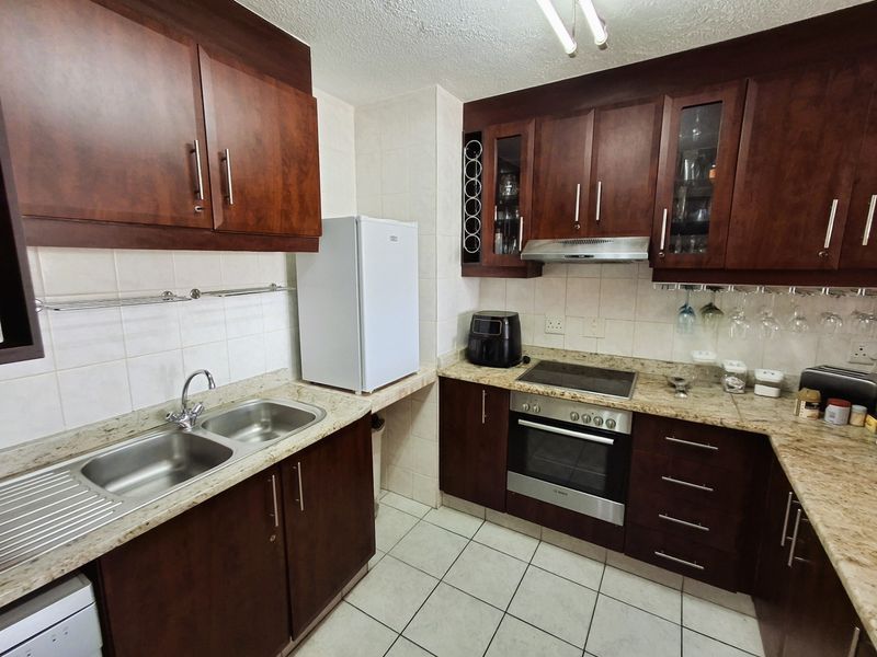 A functional kitchen featuring dark wood cabinetry, granite countertops, a double stainless steel sink, and built-in oven with electric hob.