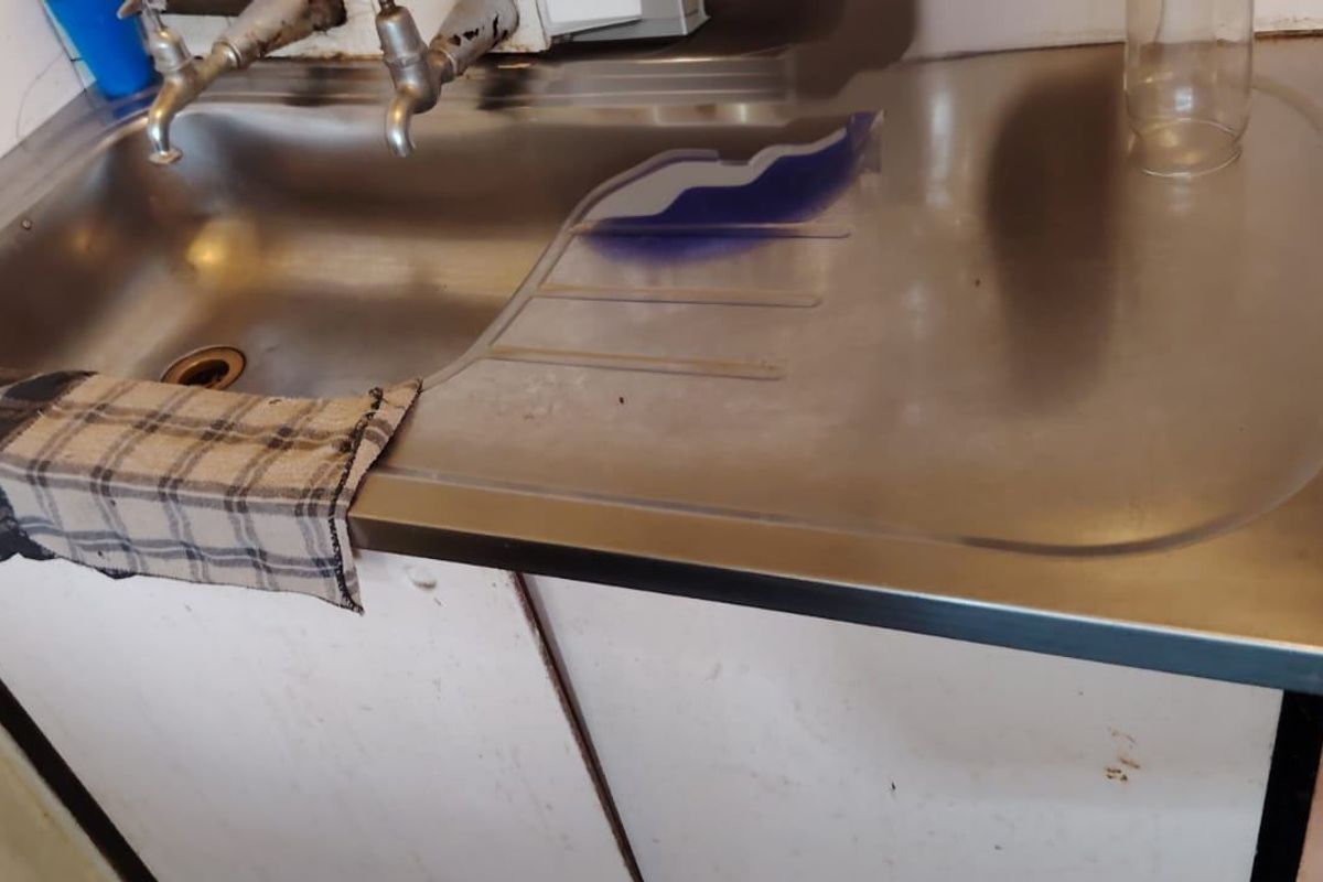 A dated kitchen area featuring a stainless steel sink, tiled splashback, and an adjacent electric stove, requiring modernization and cosmetic updates.