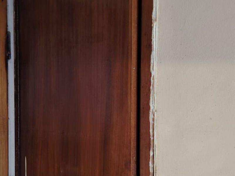 A close-up view of a built-in wooden cabinet door showing signs of wear and poor installation finish around the frame.