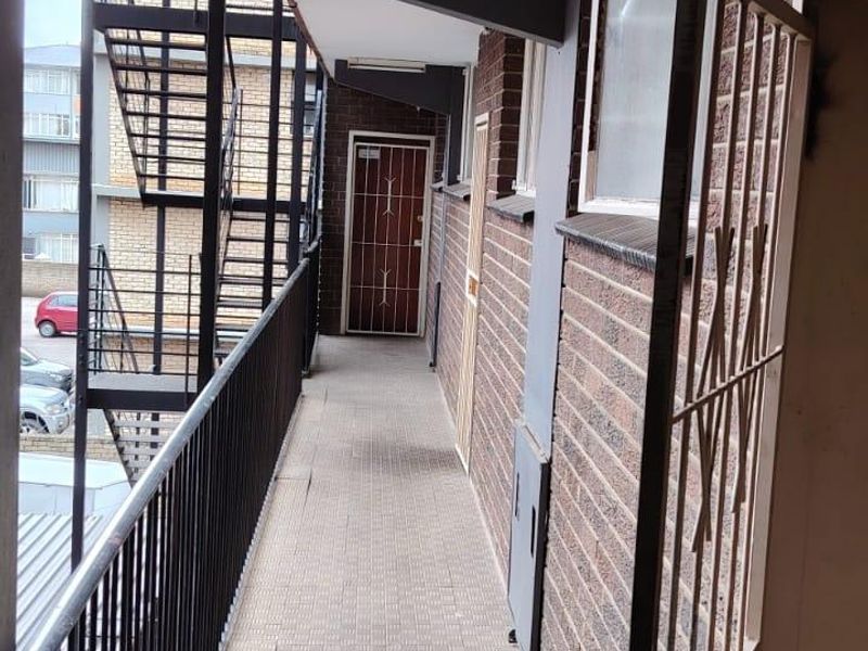 An exterior apartment access walkway featuring brick walls, tiled flooring, and a metal security gate with an adjacent external staircase.