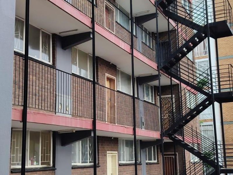 Exterior view of a multi-story apartment building featuring a prominent external steel fire escape staircase and brick facade with balcony access.