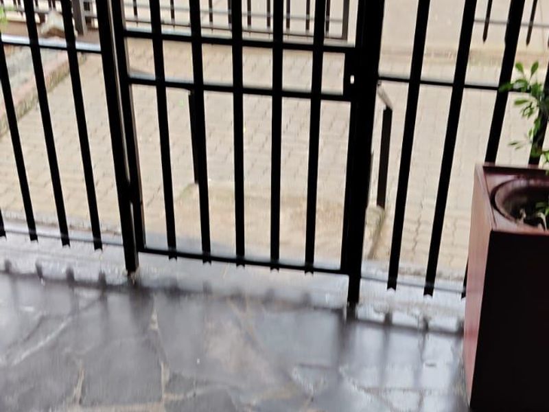 An exterior entry area featuring a security gate, stone paved flooring, and a handrail leading to the street level.