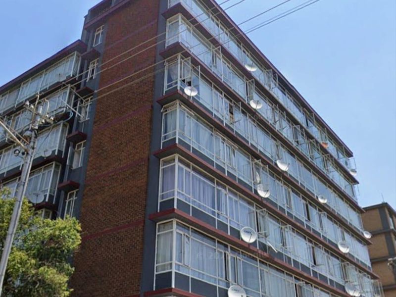 Exterior view of a multi-story apartment building featuring a brick facade and rows of enclosed balconies with aluminum window frames.