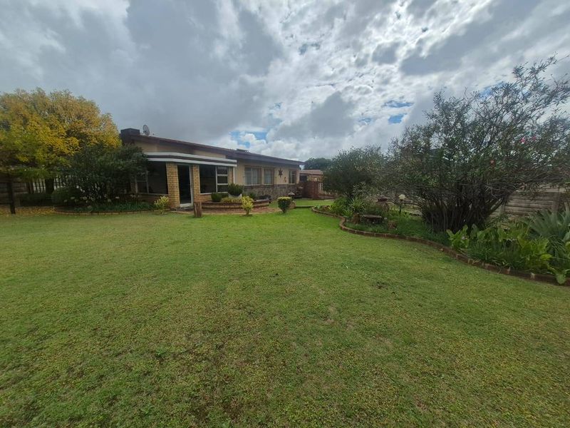 A spacious rear garden featuring a well-maintained lawn, established landscaping, and a brick-faced house exterior with a paved patio area.
