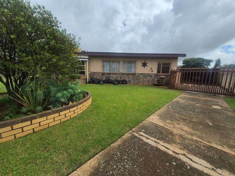 Front exterior view of the house featuring a concrete driveway, landscaped garden with a brick retaining wall, and secure gated access.