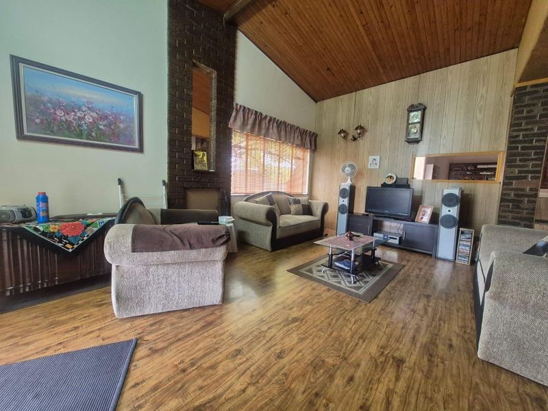 Spacious living room featuring a high timber-paneled ceiling, brick fireplace, and wood-look laminate flooring, offering a warm and traditional aesthetic.