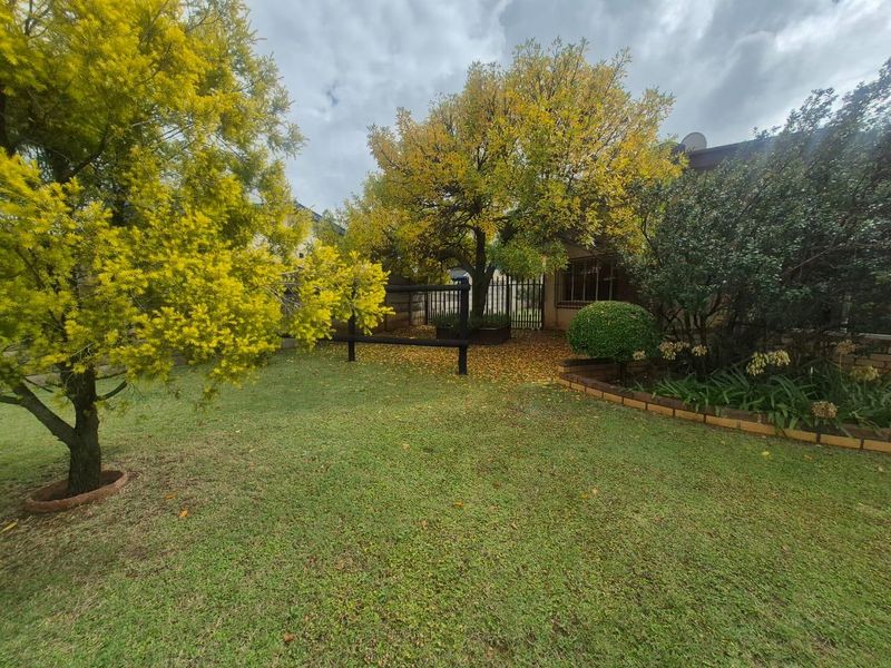 A well-established garden featuring a manicured lawn, mature trees, and brick-edged garden beds, providing a pleasant outdoor space.