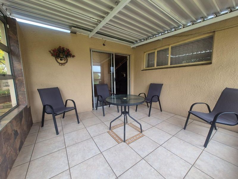A covered patio area featuring tiled flooring, a corrugated metal roof, and sliding door access to the interior living space.