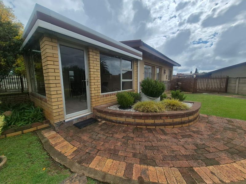 Rear exterior view featuring a paved patio area, curved brick planter, and a sunroom extension with aluminium framed windows and glass door.