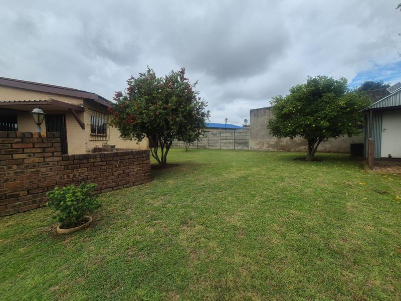 A spacious rear garden featuring a well-maintained lawn, mature trees, and a combination of brick and precast concrete boundary walls.