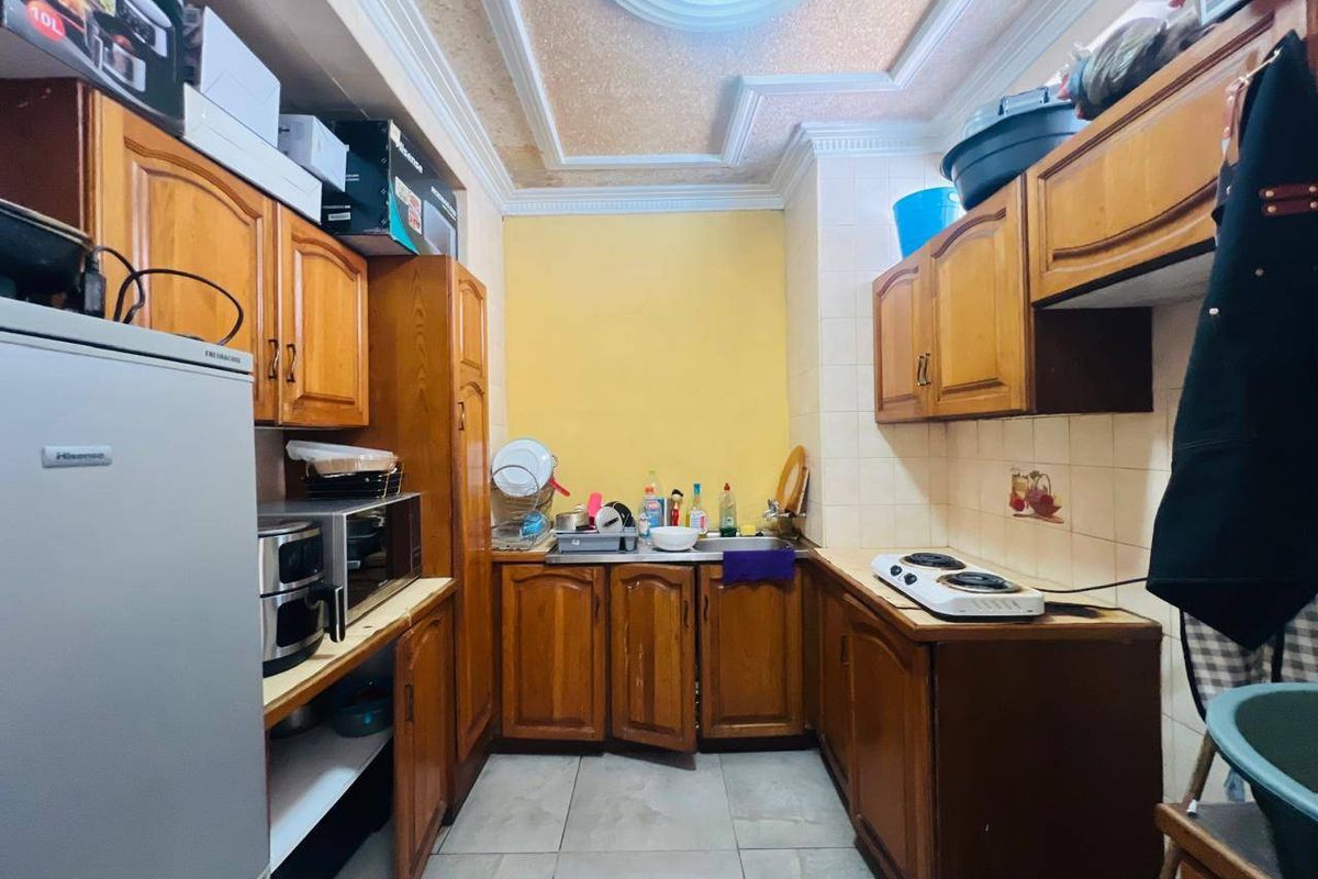 A compact kitchen featuring traditional wooden cabinetry, tiled backsplash, and tiled flooring, offering a functional layout with built-in storage and preparation space.