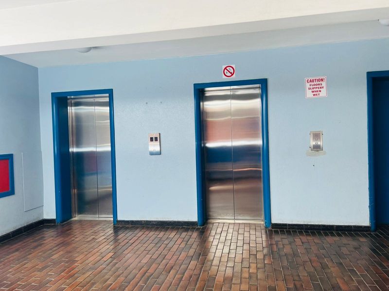 A communal apartment building hallway featuring two stainless steel elevator doors and brick-style flooring.