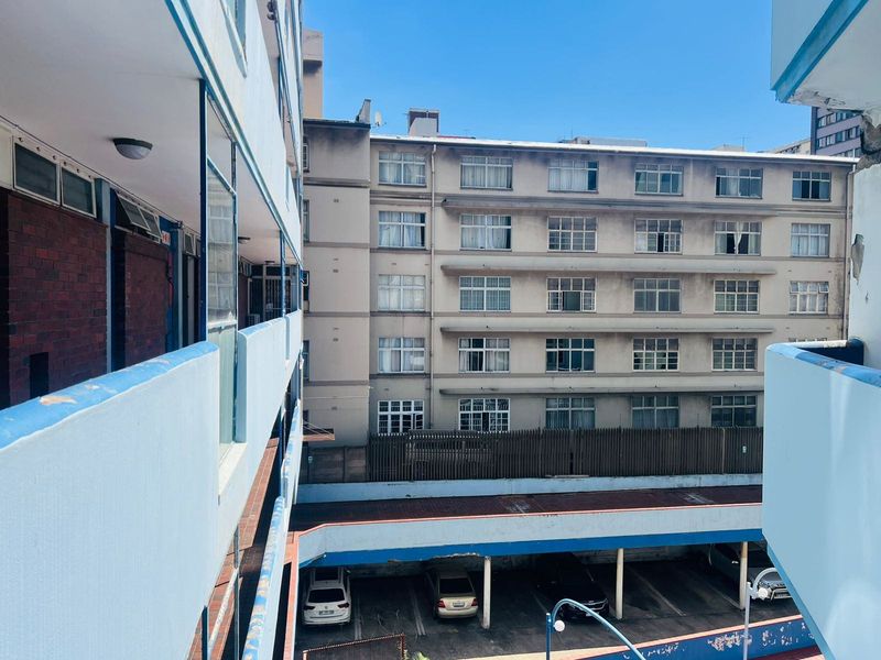 View of the apartment complex exterior, showing the building facade, balcony walkways, and ground-level parking area.