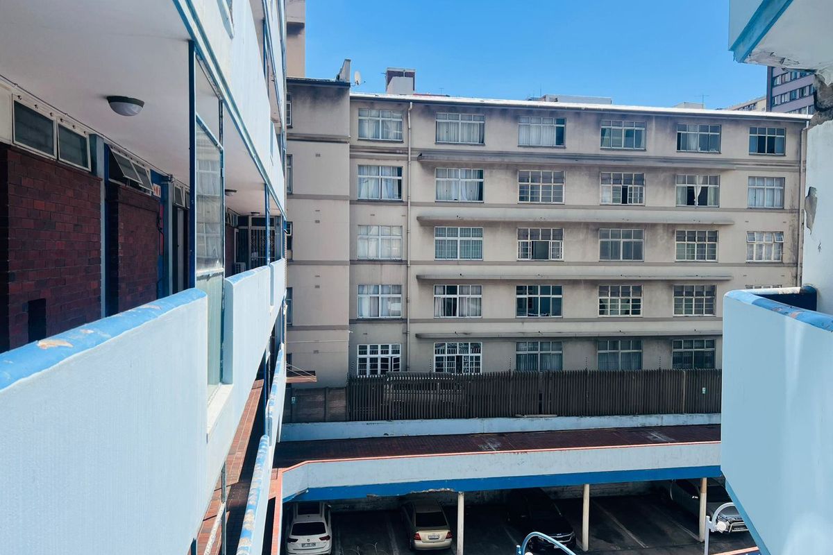 View of the apartment complex exterior, showing the building facade, balcony walkways, and ground-level parking area.