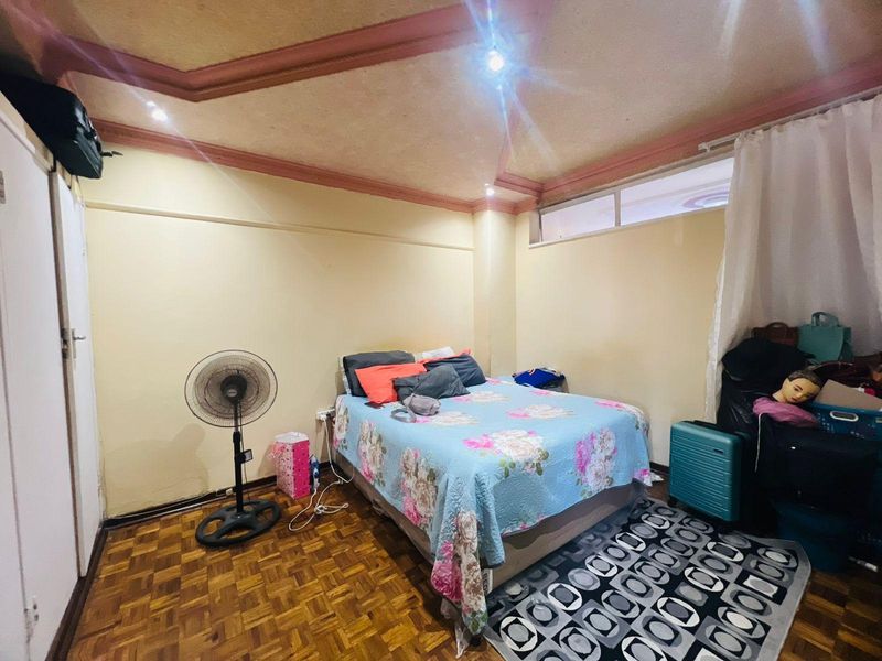 A bedroom featuring parquet flooring, decorative ceiling molding, and a high-level transom window providing natural light.